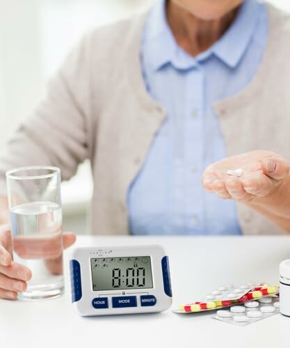 Person nimmt Tablette mit Wasser ein, Wecker auf Tisch.